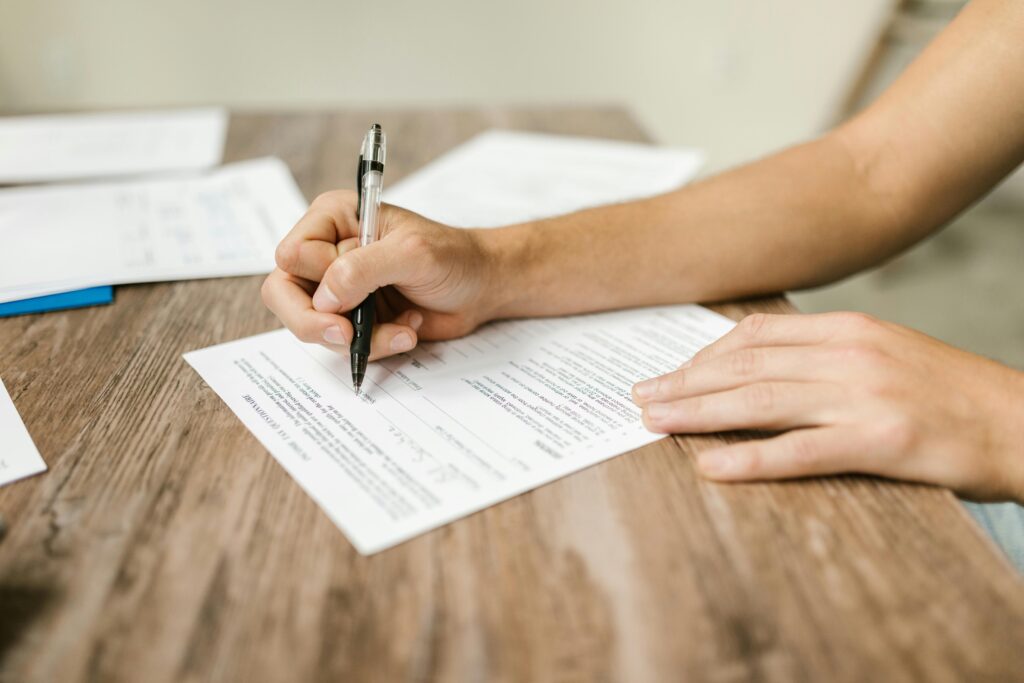 Hand filling out paperwork with a pen, showcasing focus on document completion.